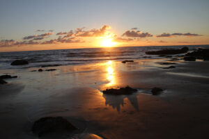 Sunset over shoreline with breaking waves.