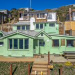 Exterior view of two story green cottage and bench seating.