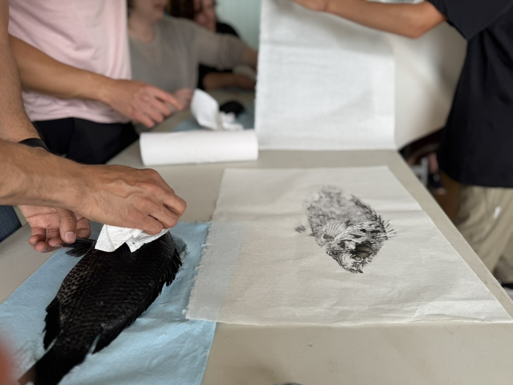 Fish covered in ink next to gyotaku print on table