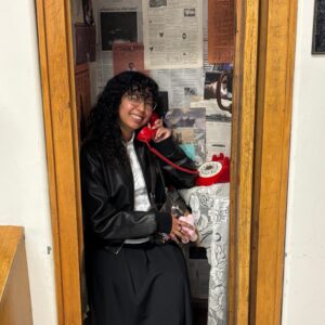 Woman sitting in a phonebooth display, holding a red phone up to her face