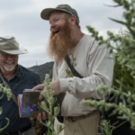 Bob Allen laughing while holding a book, standing in foliage
