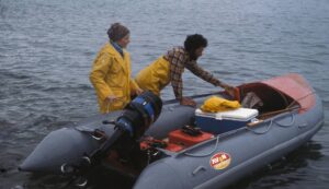 A man and woman wearing yellow rain coats loading up a small motorboat