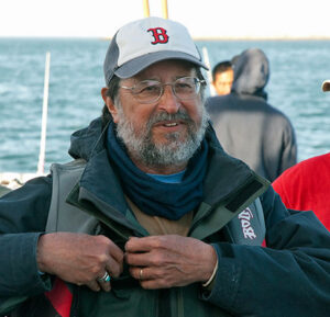 A bearded man wearing warm layers, a life jacket, and a hat while on a boat