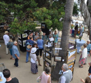 Crowd of people viewing artwork hung up on wire grids out on the beach
