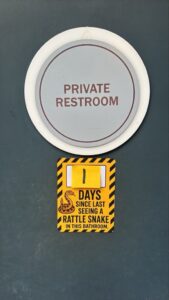 A yellow sign that reads "1 days since last seeing a rattlesnake in this restroom."