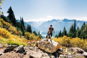 Man wearing a hat and holding walking sticks in a mountainous valley
