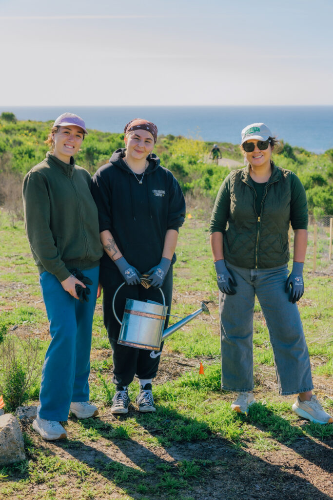 Three women in hats and gloves, smiling in a green field