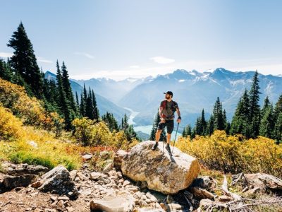Man wearing a hat and holding walking sticks in a mountainous valley
